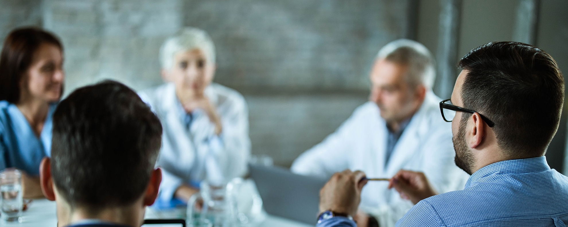 Rear view of businessmen having a business meeting with team of doctors at doctor's office. Focus is on man on the right.